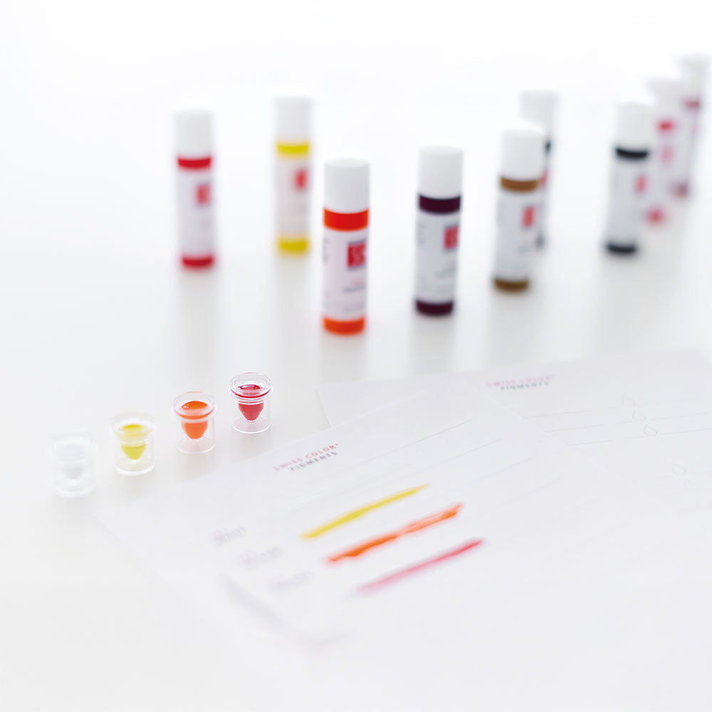 Swiss Color® permanent makeup pigment bottles and color swatches arranged on table – full pigment range for brows, lips, and correction work